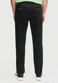 Czarne spodnie o prostym kroju, z dwiema tylnymi kieszeniami z metalowymi guzikami. Wykonane z gładkiego materiału. Noszone z białymi trampkami.