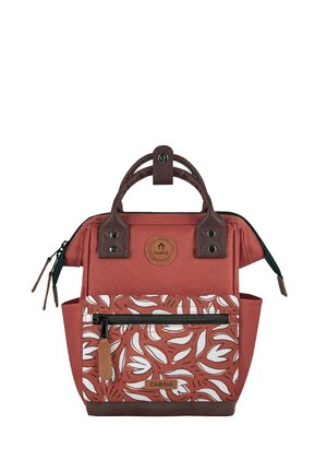 Kompakter rötlich-brauner Rucksack mit dunklen Griffen, vorderer Reißverschlusstasche mit weißem Blattmuster und kleinem Markenlogo-Patch.