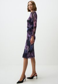 Paars lange jurk met een bloemenpatroon, gerimpelde zijkanten, slim fit en een lengte tot op de knie. Draag het met zwarte hakken.