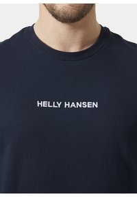 Námorně modré bavlněné tričko s kulatým výstřihem a krátkými rukávy; na hrudi má bílé vyšívané logo "HELly HANSEN".