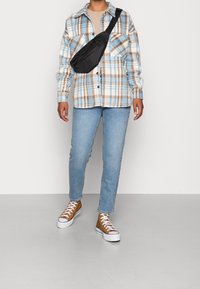 Camicia a quadri in blu chiaro, marrone e bianco, abbinata a jeans blu chiaro e sneakers marroni. Si indossa una borsa nera a tracolla.