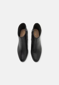 Botas de cuero negro hasta el tobillo con una textura suave, punta afilada y cremalleras laterales. El interior cuenta con una plantilla color beige con un logotipo dorado.