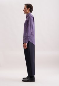 Camicia a maniche lunghe di colore viola con motivo, con polsini a bottoni, abbinata a pantaloni scuri e scarpe nere. La camicia presenta un sottile design geometrico.