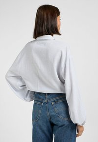 Blusa oversize a righe grigie chiaro con maniche a palloncino, dotata di colletto classico, abbinata a jeans in denim blu a vita alta.