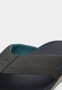 Κοντινό πλάνο καφέ και τιρκουάζ ανοιχτού πέλματος σανδαλιών με υφή στο λουρί και μαξιλαράκι στο πέλμα.