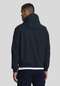 Giacca con cappuccio blu navy, caratterizzata da una vestibilità rilassata, tessuto morbido, polsini a coste e orlo dritto, con minimi dettagli di cucitura visibili.