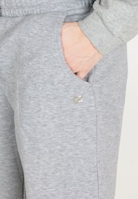 Lys grå sweatpants med en blød tekstur, der har en sidelomme og et broderet logodetalje i en kontrastfarve.
