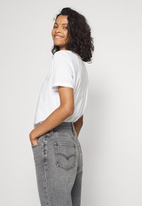 Witte t-shirt met korte mouwen gecombineerd met hooggetailleerde grijze jeans met klassieke Levi's achterzakken en een rode tab aan de zijkant.