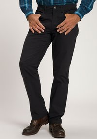 Schwarze Chinos mit einem schlanken, maßgeschneiderten Schnitt. Verfügt über vordere Taschen, einen Reißverschluss und Gürtelschlaufen. Getragen mit braunen Lederschuhen.