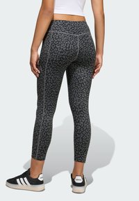 Čierne legíny so sivým leopardím vzorom, majú hladkú textúru a priliehavý strih, skombinované s čiernymi teniskami s bielymi detailmi.
