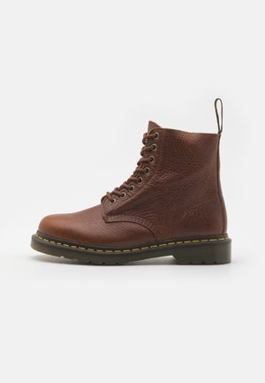 Bottine en cuir marron à lacets avec une semelle noire épaisse et des surpiqûres jaunes, dotée d'une languette à l'arrière.