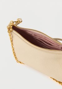 Sac en cuir beige clair avec une surface texturée, une fermeture éclair dorée et une bandoulière en chaîne. L'intérieur comprend une doublure rose et plusieurs emplacements pour cartes.