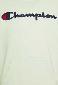 Světle zelená mikina s kapucí a přední kapsou, na hrudi s vyšitým nápisem "Champion" v černé a červené barvě. Hladká, texturová tkanina.