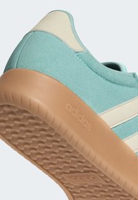 Turquoise sneaker with a textured fabric upper, cream accents, and a gum rubber sole featuring an embossed logo.