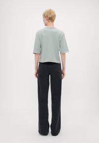 Lys grønn, kortermet t-skjorte med crop fit, kombinert med høytliv, løstsittende sorte jeans; minimalistisk design, ingen synlige mønstre.