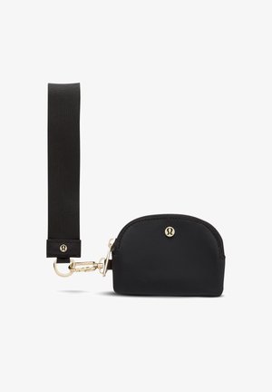 Kleine schwarze Reißverschlusstasche mit goldfarbenem Verschluss und schwarzem Stoffhandgelenkband, mit kleinem goldenem rundem Logo vorne.