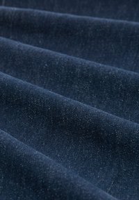 Tamno plavi denimski materijal s mekom teksturom, s vidljivim tkanjem i blagim sjajem, uređen u presavijenim slojevima.