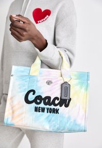 Sac fourre-tout en toile aux couleurs pastel tie-dye avec un logo noir « Coach New York », léger, doté de doubles anses et d'une étiquette métallique.
