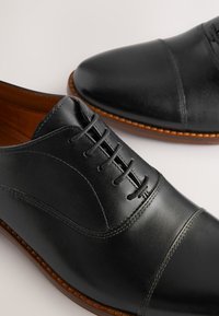 Schwarze Lederschuhe mit runder Spitze, Schnürverschluss und kontrastierender brauner Sohle, sichtbaren Nähten und glatter Textur.