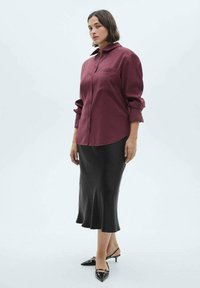 Burgundy knäppskjorta med långa ärmar, kombinerad med en figursydd svart midikjol och svarta pumps med spetsig tå. Slät, lättviktsmaterial.