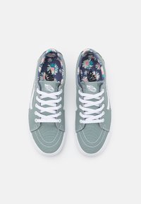 Des baskets en toile vertes avec des lacets blancs, présentant une semelle intérieure à motif floral et des coutures contrastées sur le dessus.