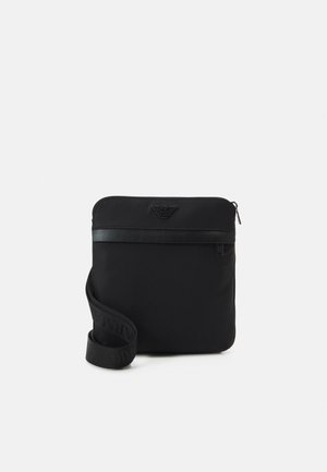 Sort rektangulært crossbody taske med lynlås, justerbar rem og præget mærkelogo på frontpanelet.