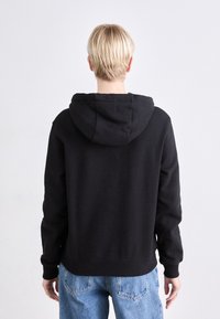 Felpa nera con cappuccio, dal taglio morbido, con polsini e orlo a costine. Tessuto liscio, caratterizzata da un design semplice e priva di loghi o dettagli visibili.