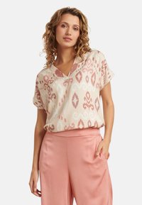 Short-sleeve top in light pink and cream with an ikat pattern. Features a V-neckline and flowing design, paired with blush wide-leg pants.