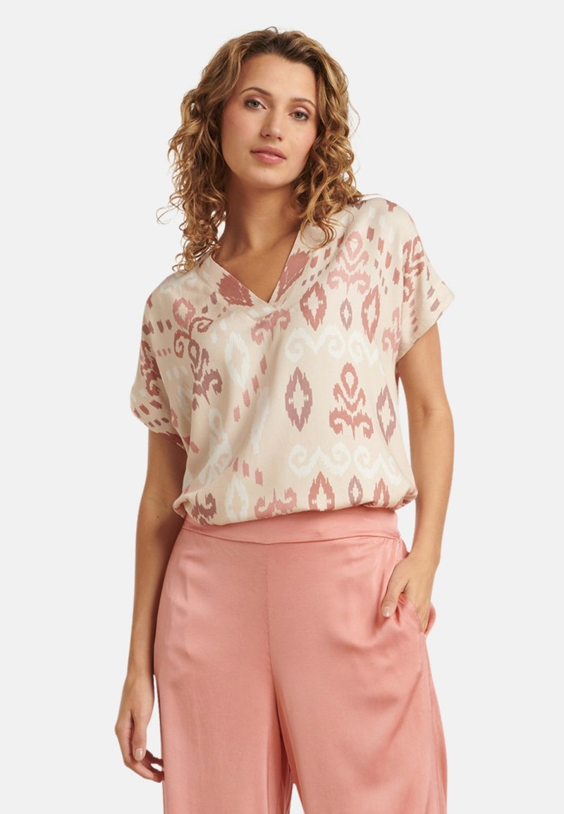 Short-sleeve top in light pink and cream with an ikat pattern. Features a V-neckline and flowing design, paired with blush wide-leg pants.