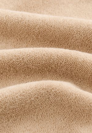 Mehka, bež flis tkanina v gladkih, teksturiranih gubah, ki razkazujejo fino, gosto, puhasto površino z rahlimi odtenki barv.