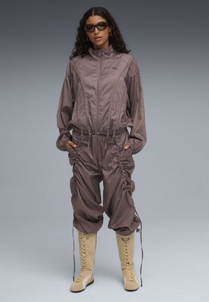 Tuta Puma in lavanda tenue con zip frontale, dettagli arricciati e tasche laterali. Abbinato a stivali beige alti fino al ginocchio.