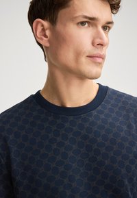 Felpa blu navy con un motivo circolare in rilievo ripetuto di un marrone più chiaro; colletto a costine; materiale morbido.