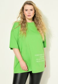 Una camiseta de gran tamaño en un brillante color verde, hecha de un tejido suave, con mangas cortas y un diseño de texto impreso en blanco en la parte delantera.