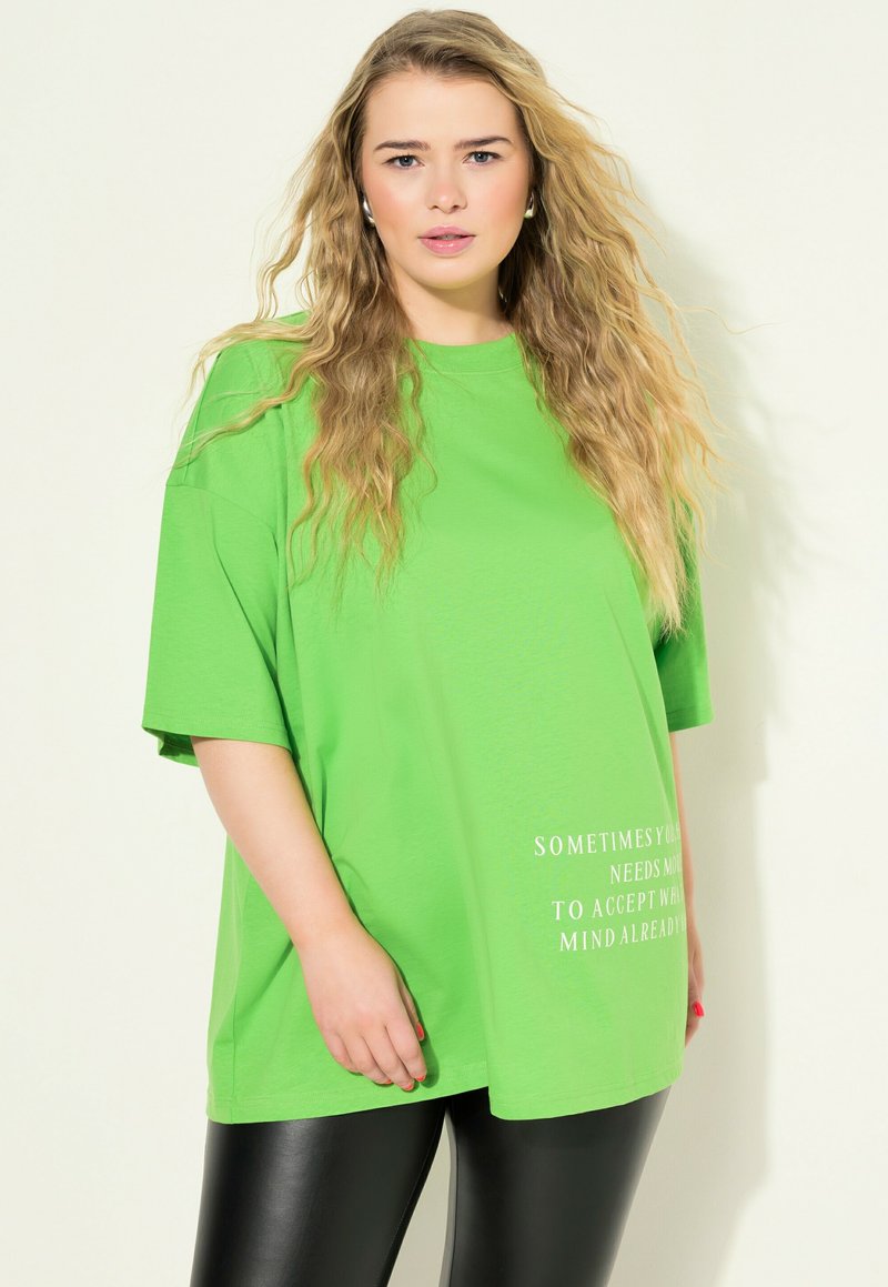 Una camiseta de gran tamaño en un brillante color verde, hecha de un tejido suave, con mangas cortas y un diseño de texto impreso en blanco en la parte delantera.