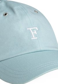 Gorra de color azul claro hecha de tela con un acabado texturizado, que presenta un logotipo bordado en blanco con la letra "F" y ojales de metal para ventilación.