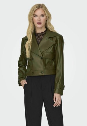 Chaqueta corta de imitación piel verde con botones de doble pecho, solapas con muesca y un bolsillo. Combinada con pantalones negros. Textura suave.