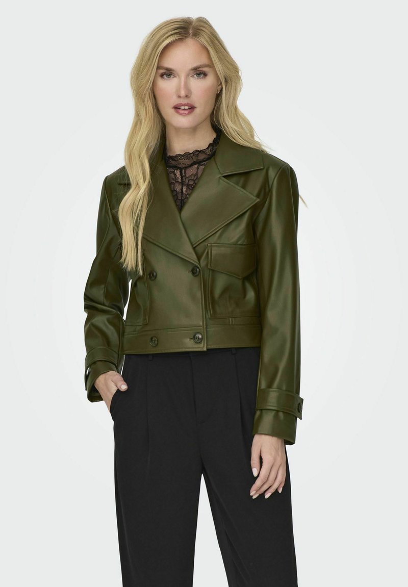 Giacca corta in finta pelle verde con bottoni doppi, rever a scollatura e una tasca. Abbinata a pantaloni neri. Texture liscia.