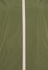 Veste verte olive avec une texture lisse, dotée d'une fermeture éclair rose clair contrastante au centre. Design simple, sans motifs ni accents supplémentaires.