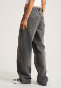 Graue, weit geschnittene Jeans aus Denim, mit einer hohen Taille, Gesäßtaschen und einer weichen Textur, kombiniert mit schwarz-weißen karierten Sneakers.