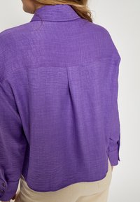 Lilla, struktureret skjorte med knapmanchetter og krave. Har en læg bagpå, med en afslappet, løs pasform og letvægtsstof.