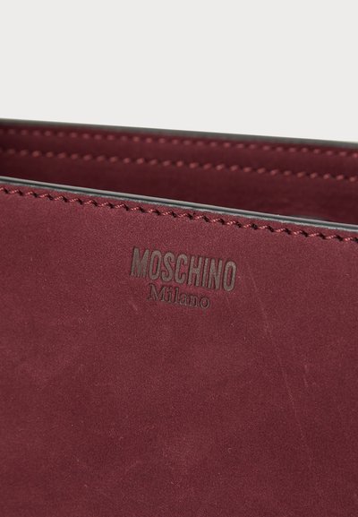Didelis raudonasis odinis piniginė su įspaustu "Moschino Milano" logotipu, pasižyminti lygiu paviršiumi ir kontrastingomis siūlėmis.
