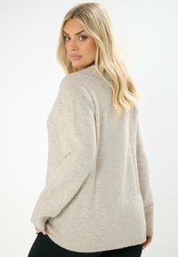 Beiger Pullover mit lässiger Passform, gerippten Bündchen und einem leicht abgerundeten Saum. Weiche Textur und dezentes Muster über das gesamte Kleidungsstück.