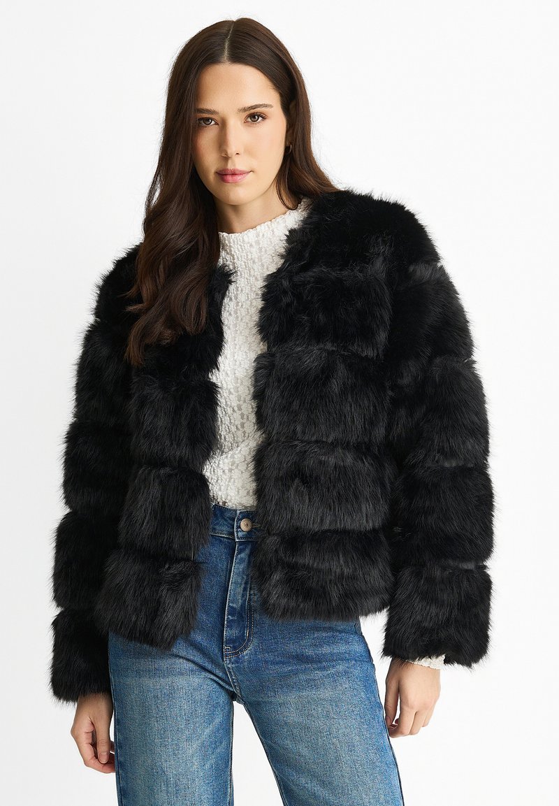 Black faux fur cropped jacket with horizontal stripes, featuring a soft texture and a relaxed fit, worn over a light sweater and jeans.