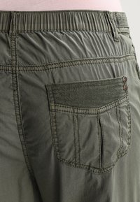 Gröna byxor med en samlad elastisk midja, med en texturerad bakficka och kontrasterande sömnadsdetaljer. Materialet verkar vara lätt.