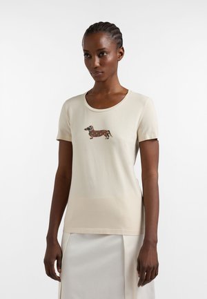 Nainen, jolla on päällään beige lyhythihainen t-paita, jossa on kuvioitu mäyräkoiran kuva rinnan keskellä, ja vaalea hame.