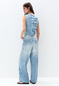 Jeansblus med rynkdetaljer på baksidan, kombinerad med löst sittande ljusblå jeans med en urtvättad finish och distinkta fickor.