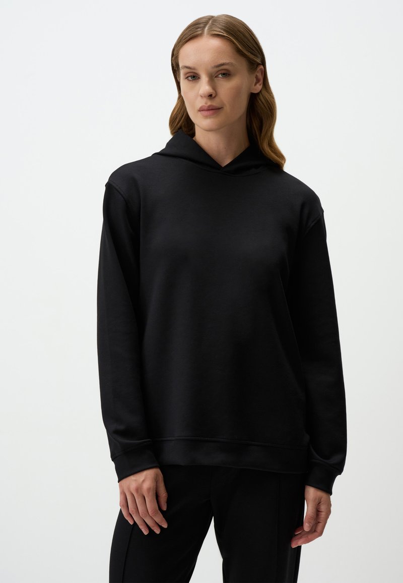 Czarna bluza z kapturem o miękkiej teksturze, z regulowanym kapturem, długimi rękawami i luźnym krojem. Dodatki obejmują ściągacz u dołu oraz przy mankietach.