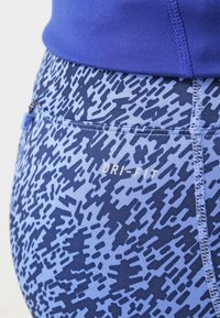 Niebieskie legginsy sportowe z logo Dri-FIT, z teksturowanym wzorem w ciemniejszym odcieniu niebieskiego, dopasowanym kroju i widocznymi detalami szwów.