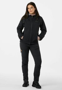 Giacca nera da esterno con cappuccio, chiusura con zip e polsini elasticizzati; abbinata a pantaloni neri con più tasche e una finitura testurizzata.