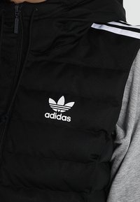 Black insulated vest with a zip closure, featuring a hood, grey sleeve accents, and a white Adidas logo on the front.